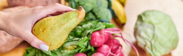 hand of vegetarian woman with delicious pier above blurred vegetables and fruits, horizontal banner