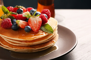 Delicious pancakes with fresh berries, honey and butter on grey table, closeup