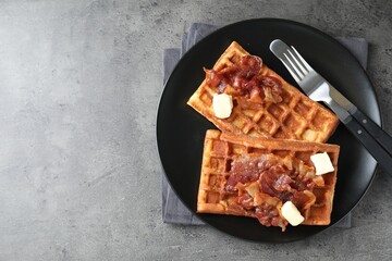 Tasty Belgian waffles served with bacon and butter on grey table, top view. Space for text
