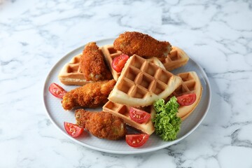Tasty Belgian waffles served with fried chicken, tomatoes and lettuce on white marble table