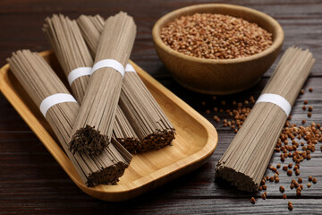 Uncooked buckwheat noodles (soba) and grains on wooden table, closeup