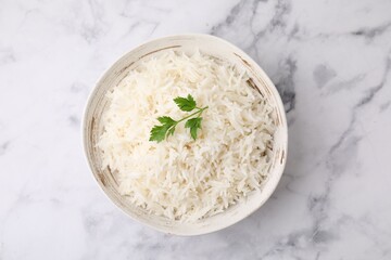 Bowl of delicious rice with parsley on white marble table, top view