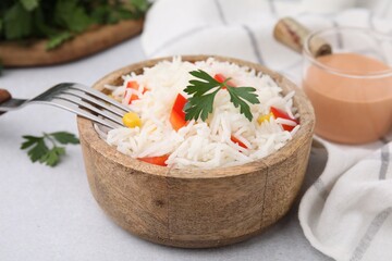 Bowl of delicious rice with vegetables and parsley served on light gray table, closeup