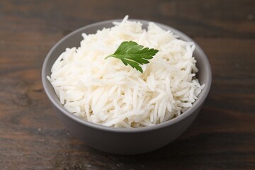Bowl of delicious rice with parsley on wooden table, closeup