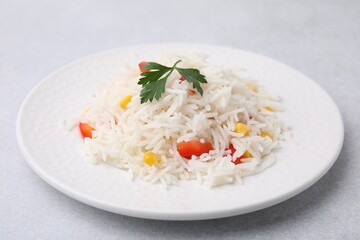 Delicious rice with vegetables and parsley on light gray table, closeup