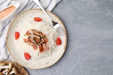 Delicious rice with bacon, mushrooms and tomatoes served on gray table, flat lay. Space for text