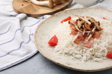 Delicious rice with bacon, mushrooms and tomatoes on table, closeup