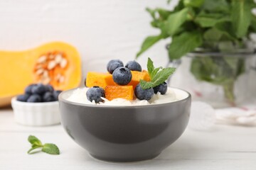 Bowl of delicious rice porridge with blueberries, pumpkin and mint on white table, closeup