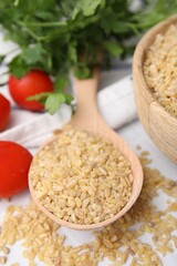 Spoon with raw bulgur and tomatoes on table, closeup