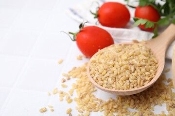 Spoon with raw bulgur and tomatoes on table, closeup. Space for text