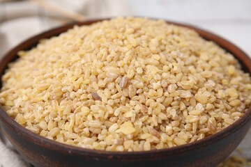 Raw bulgur in bowl on table, closeup