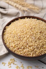 Raw bulgur in bowl on white wooden table, closeup