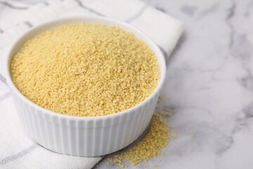 Raw couscous in bowl on light table, closeup