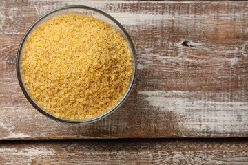 Raw bulgur in bowl on wooden table, top view. Space for text