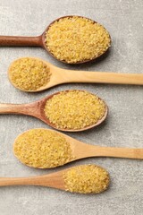 Spoons with raw bulgur on gray table, flat lay