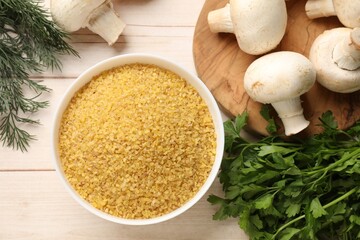 Raw bulgur in bowl, herbs and mushrooms on light wooden table, flat lay