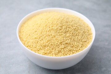 Raw couscous in bowl on gray table, closeup
