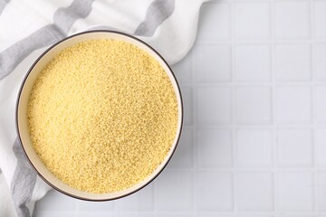 Raw couscous in bowl on white tiled table, top view. Space for text
