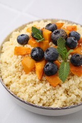Bowl of tasty couscous with blueberries, pumpkin and mint on table, closeup