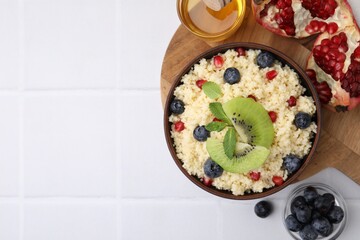 Bowl of tasty couscous with kiwi, blueberries, pomegranate and honey on white table, flat lay. Space for text