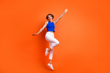 Full size photo of active overjoyed girl jumping have good mood empty space isolated on orange...