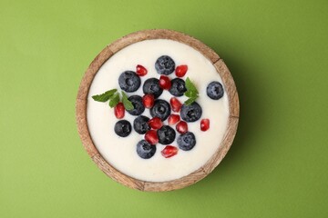 Bowl of delicious semolina pudding with blueberries, pomegranate and mint on green background, top view