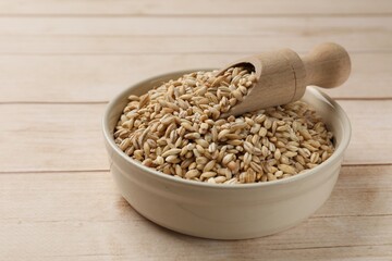 Dry pearl barley in bowl and scoop on light wooden table, closeup