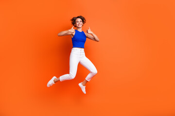 Fototapeta na wymiar Full body photo of active carefree lady jump demonstrate thumb up empty space ad isolated on orange color background