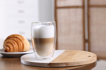 Aromatic latte macchiato in glass and croissant on wooden table against blurred background. Space for text