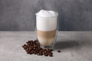 Aromatic latte macchiato in glass and coffee beans on light grey table
