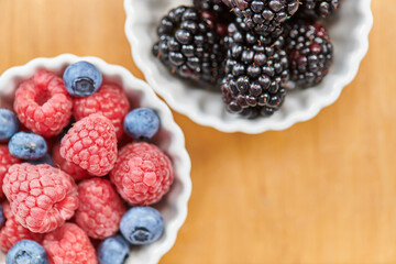 close up of ripe blackberries and blueberries with raspberries in bowls, delicious vegetarian diet