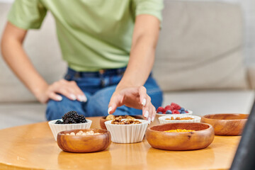 cropped blurred woman taking bowl of walnuts near fresh berries and legumes on table, vegetarianism