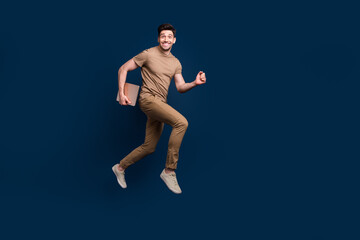 Fototapeta na wymiar Full size photo of funny energetic man dressed beige t-shirt running to empty space hold laptop isolated on dark blue color background