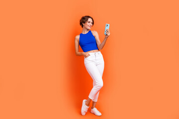 Full body photo of stunning positive lady hold use smart phone typing blog post isolated on orange color background