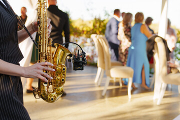 A woman musician plays the saxophone at an open-air party.  - obrazy, fototapety, plakaty