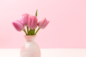 Vase with bouquet of tulip flowers in front of pink background. Composition in pastel colors.