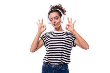 young positive curly brunette woman in a striped casual t-shirt listens to music in headphones