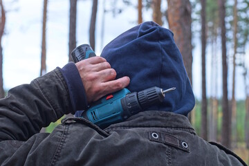 the hand of a male worker in a gray jacket and a blue hood holds a screwdriver on his shoulder on...
