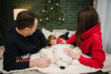 Concept of family holiday. Father, mother hug son lying on bed at home. Happy New Year and Merry Christmas. Family play with child. Mom, dad embrace kid. Christmas tree, decorated interior. Closeup.