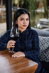 Elegant young Asian woman with glass of red wine sitting by the table in restaurant alone