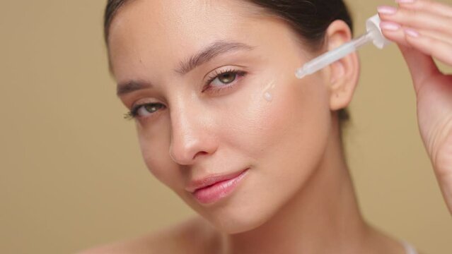 Young beautiful woman applying face serum with pipette on her face close up. Cosmetic procedures for facial skin care