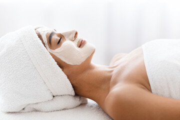 Obraz na płótnie Canvas Side view indian woman applying facial clay mask at spa