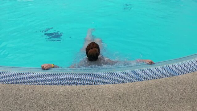 Woman is enjoying swimming in the outdoor pool and getting a massage on the underwater massage attraction.