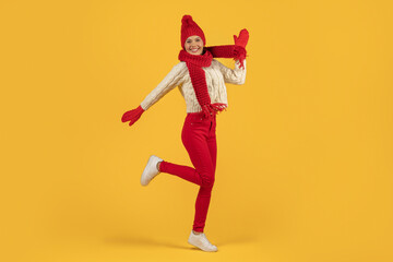 Fototapeta na wymiar Joyful woman in red knitted hat jumping on yellow backdrop