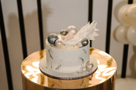 Trendy baptism cake with figure newborn, wings angel and silver decor. Cake on background luxury photo zone. Celebration baptism concept. Delicious reception at birthday baby party. Closeup.