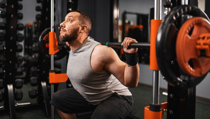 A large bearded man in the gym performs a squat exercise with a barbell. Preparation of a...