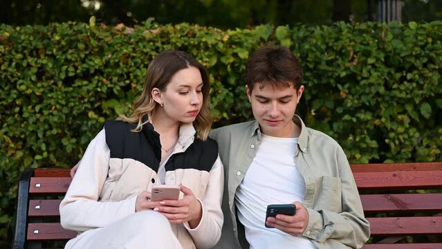 A jealous woman peeks at her boyfriend's phone while relaxing on a park bench. Close up
