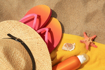 Fototapeta na wymiar Straw hat, flip flops and other beach items on sand, flat lay