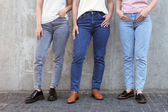 Women in stylish jeans near grey wall outdoors, closeup