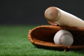 Baseball bat, leather glove and ball on green grass against dark background, closeup. Space for text